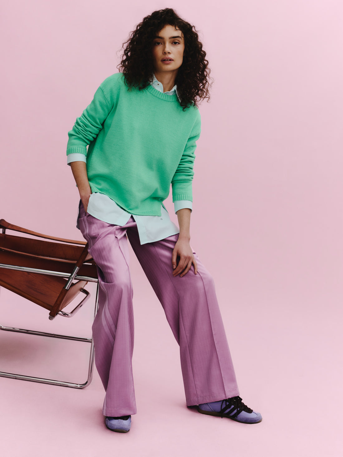 Woman wearing a green sweater and purple pants on a pink background